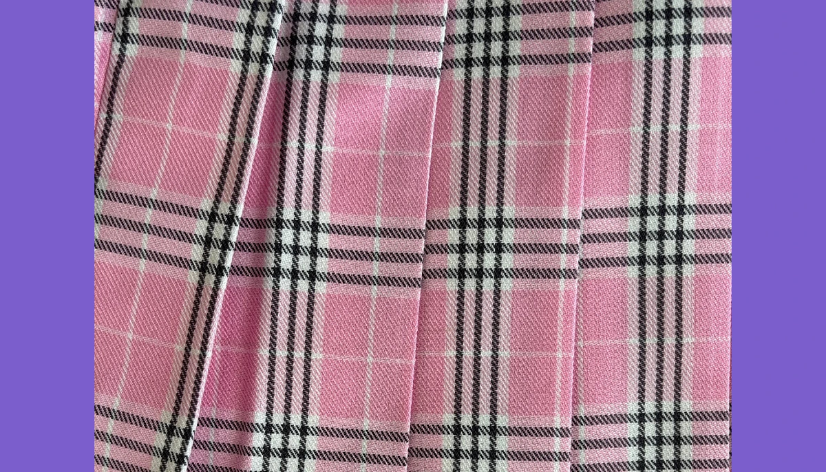 Pink plaid fabric with black and white stripes, shown in a close-up folded view against a purple background.