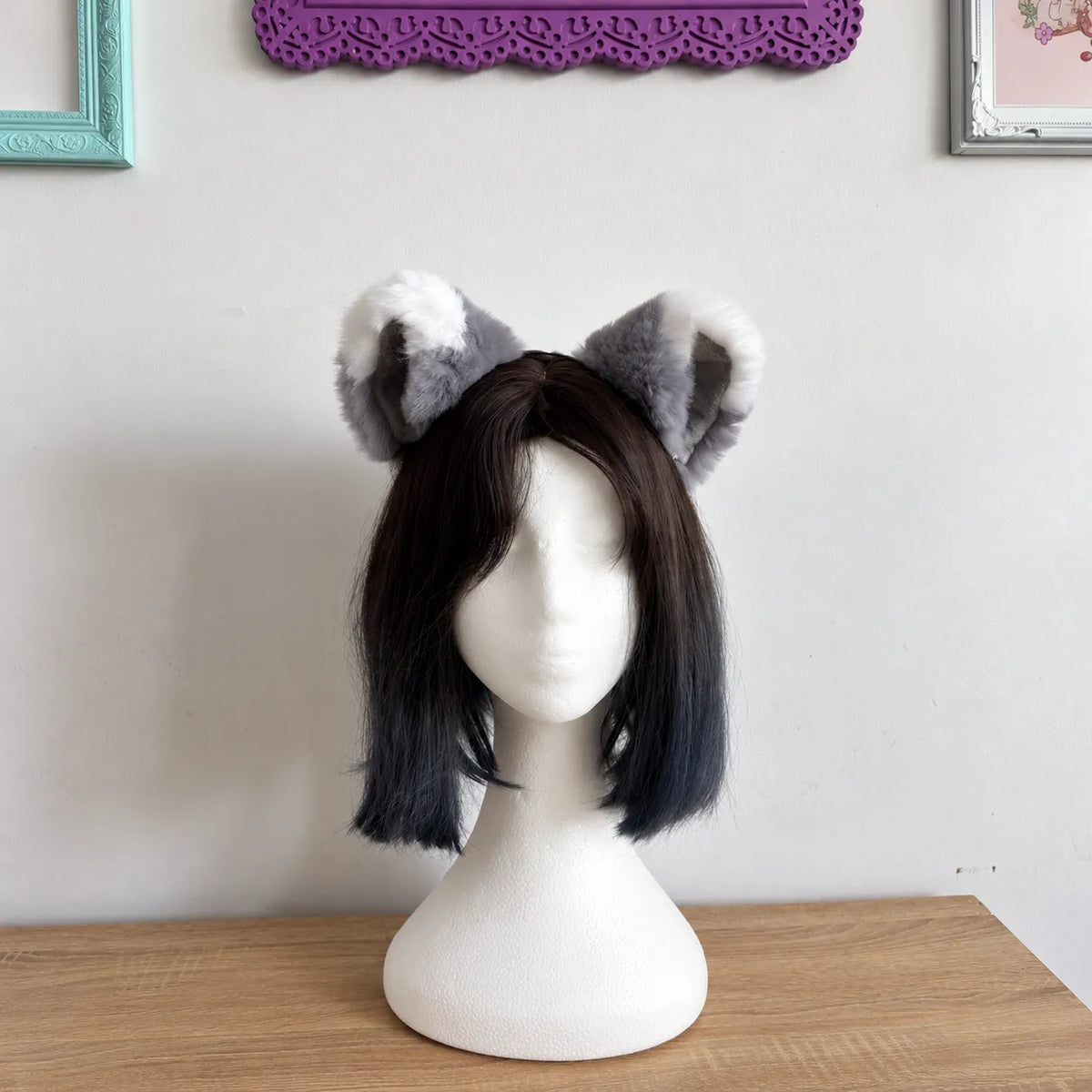 Grey and white furry animal ears on a white mannequin head, displayed on a wooden table against a light wall with framed pictures.